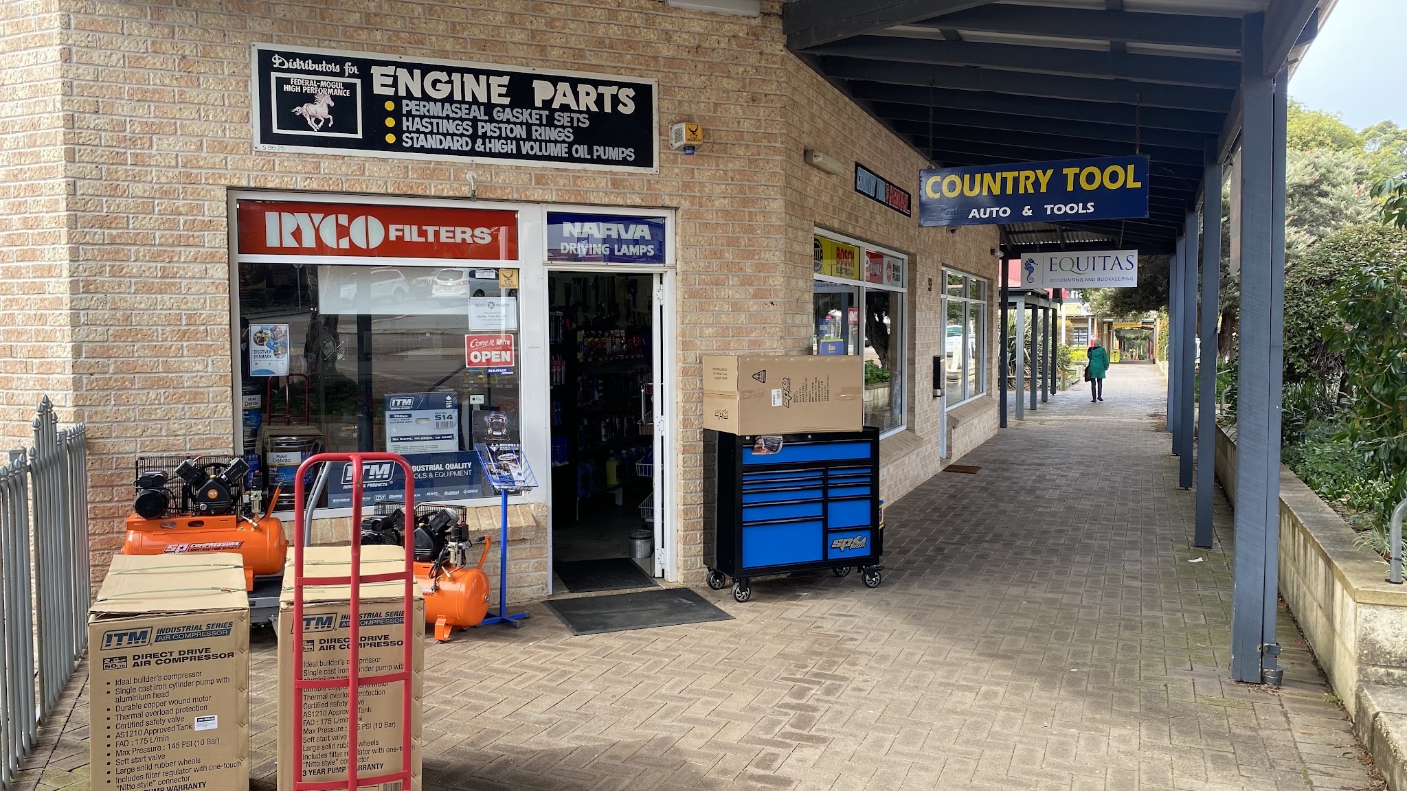 The front door of Country Tool & Auto, with the Federal-Mogul engine parts board above it and air compressors on the footpath
